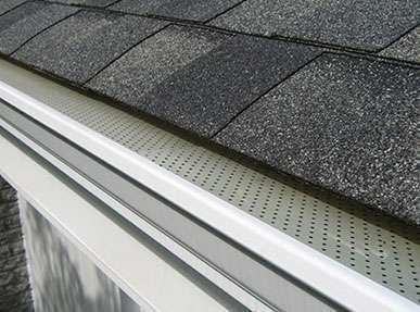 Perforated metal screen gutter guard on a white gutter under dark gray shingles