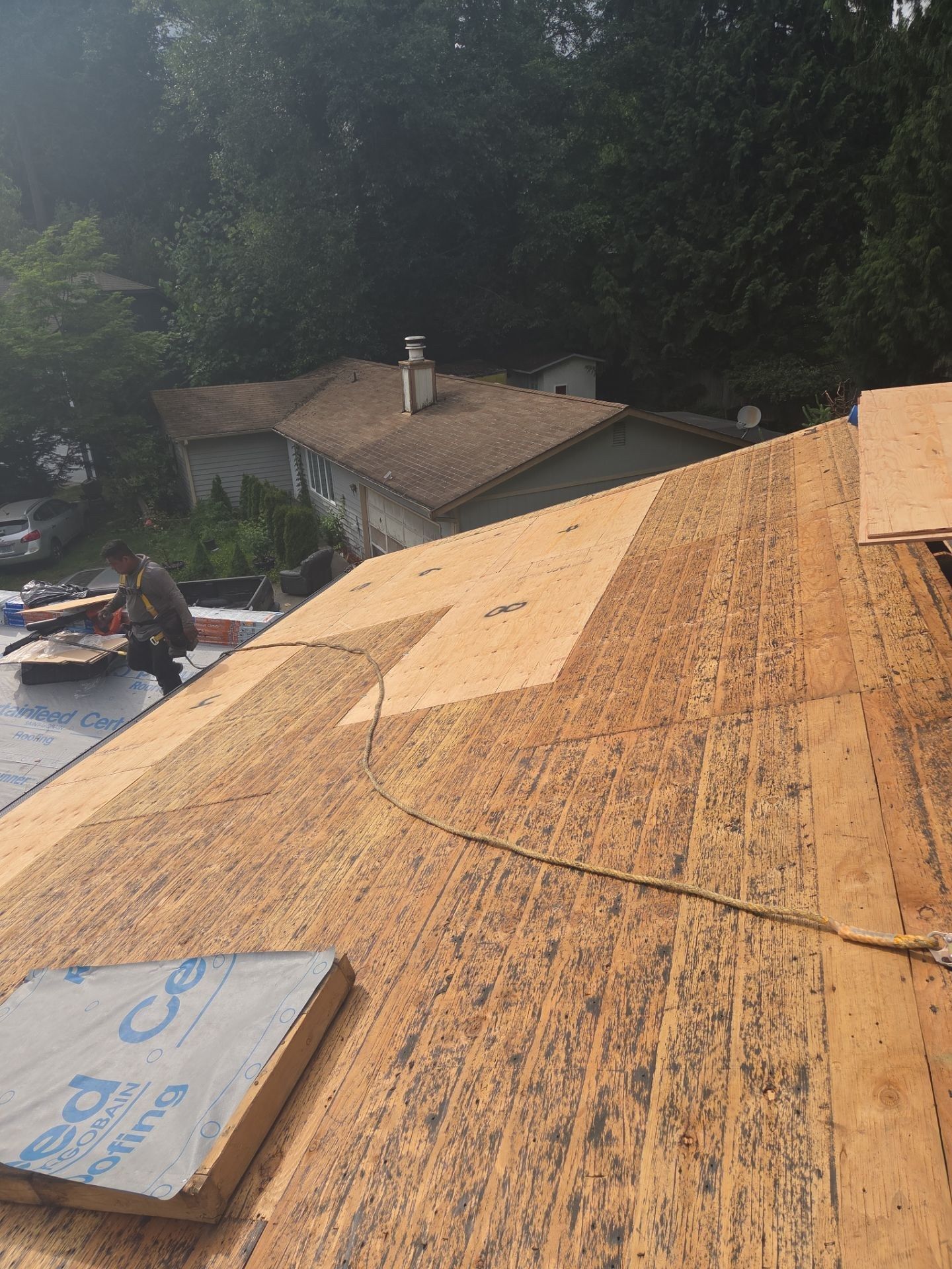 Roof stripped to the wood deck during a tear-off, with lighter new sheathing panels patched in and a roofer working at the eave