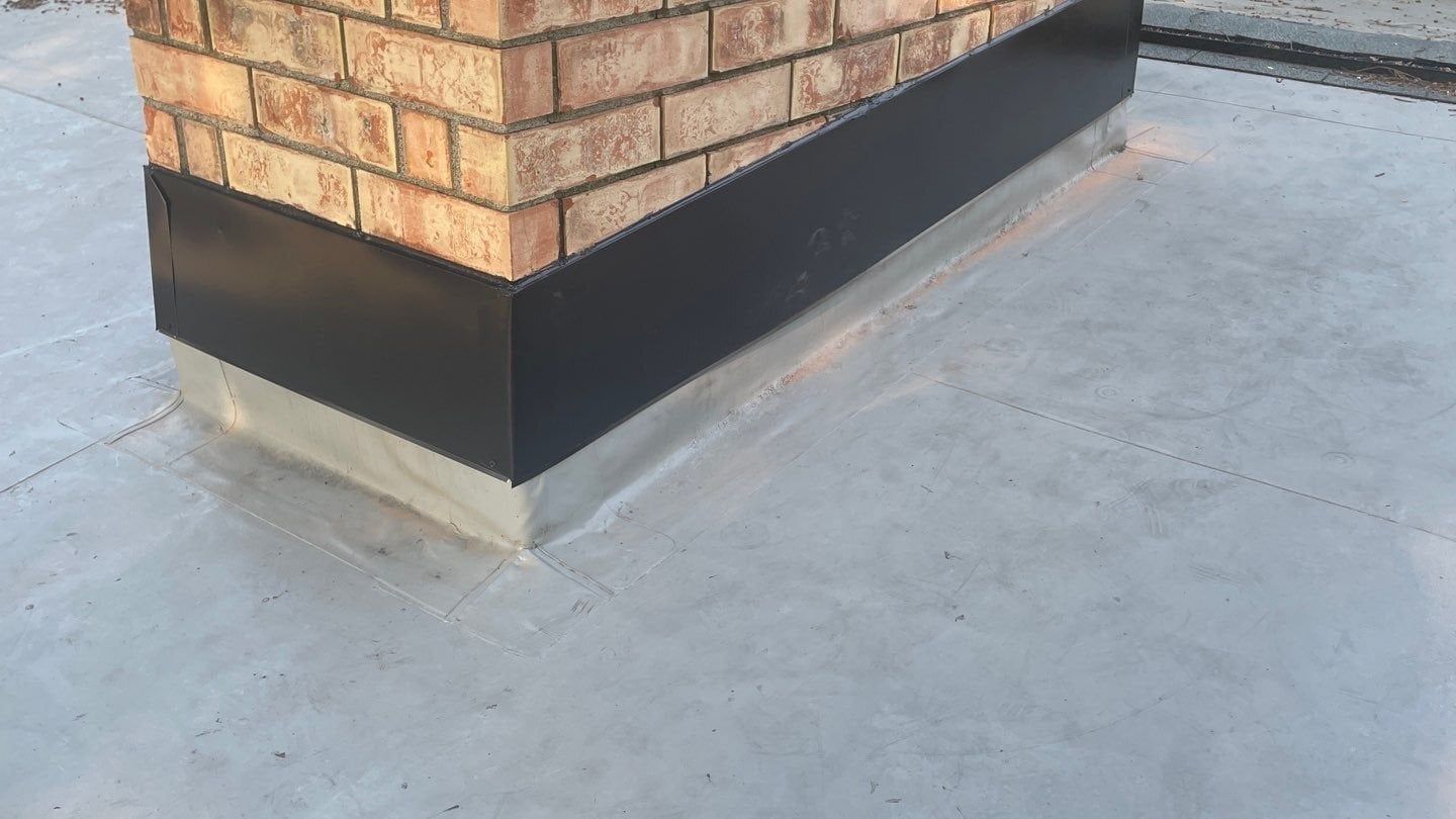 Finished PVC flat roof with black metal counterflashing around a brick chimney in Tukwila