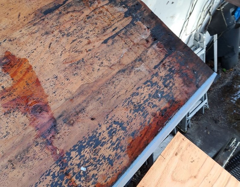 Roof decking with water damage along the edge during a tear-off, next to a new plywood sheet
