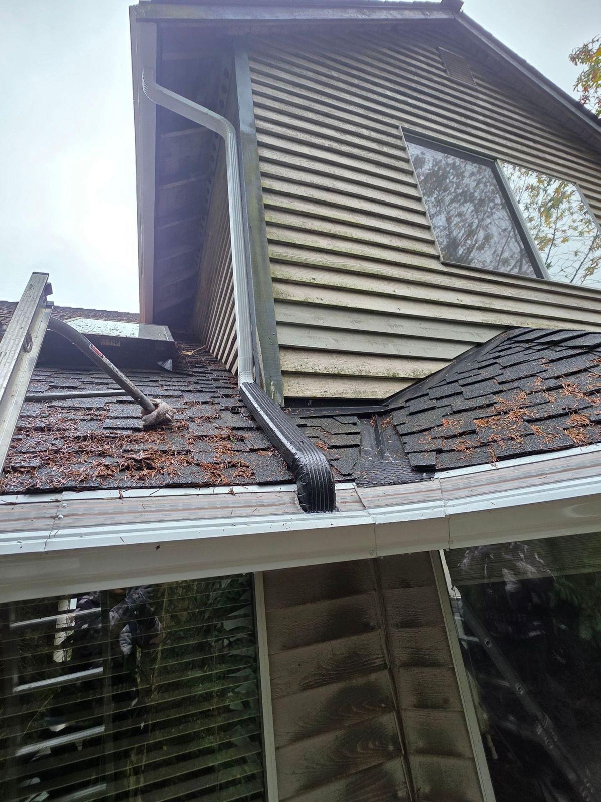 New white downspout running down the second-story wall and tied in at the gutter on the lower roof